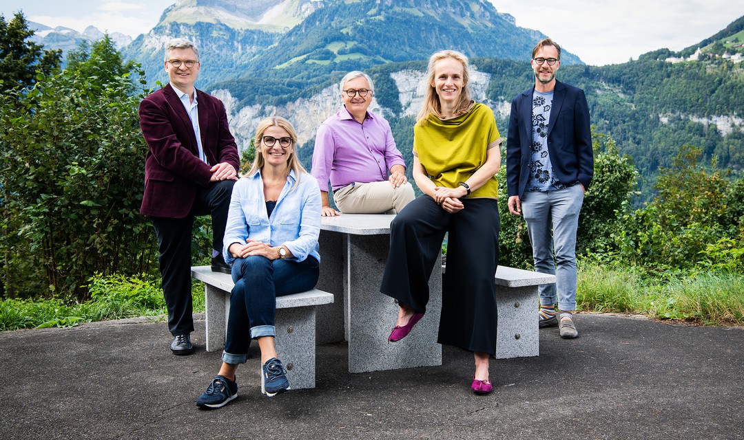 Gruppenbild vom neuen «Wort zum Sonntag»- Team. Im Hintergrund sind Berge und Natur. Das Team sitzt auf einem Tisch und auf den Bänken.