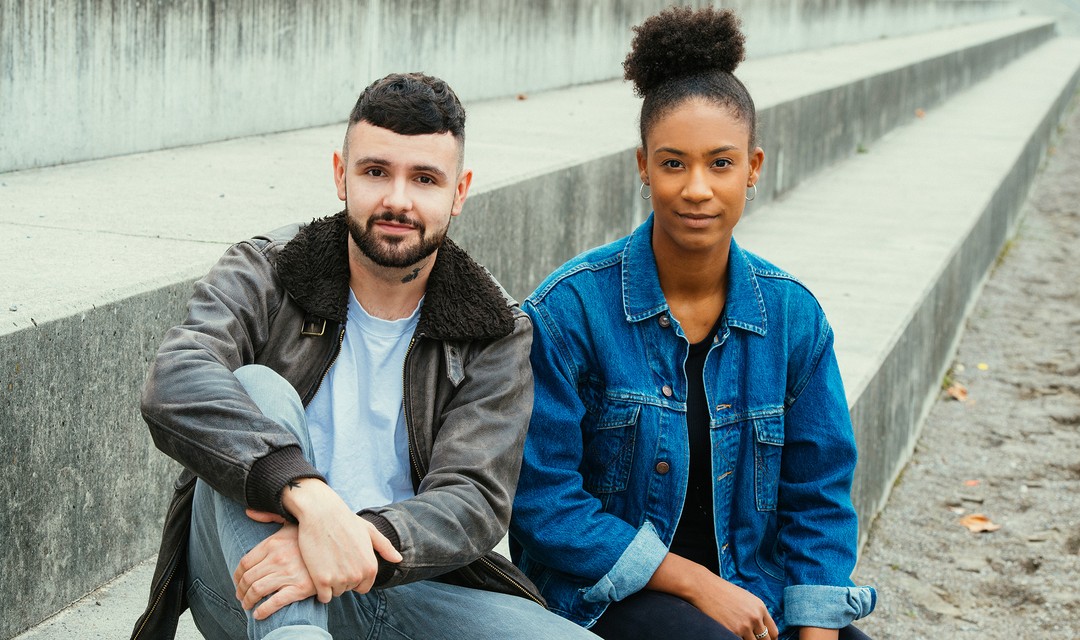 Die beiden Hosts Livio und Lena im Porträt. Sie sitzen nebeneinander.