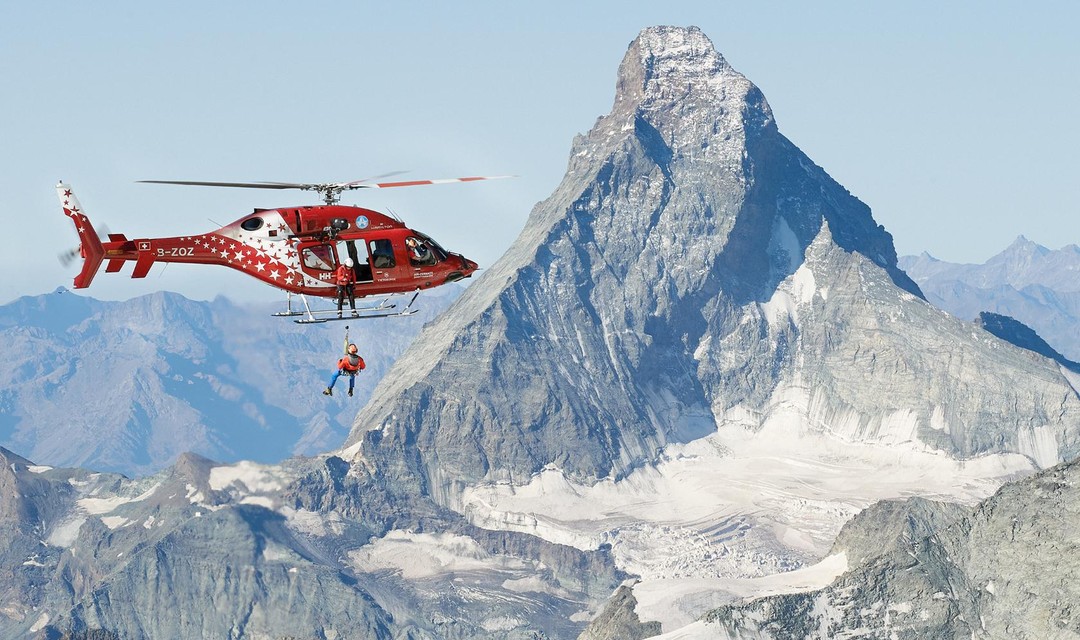 Ein Helikopter der Rega vor einem Berggipfel.