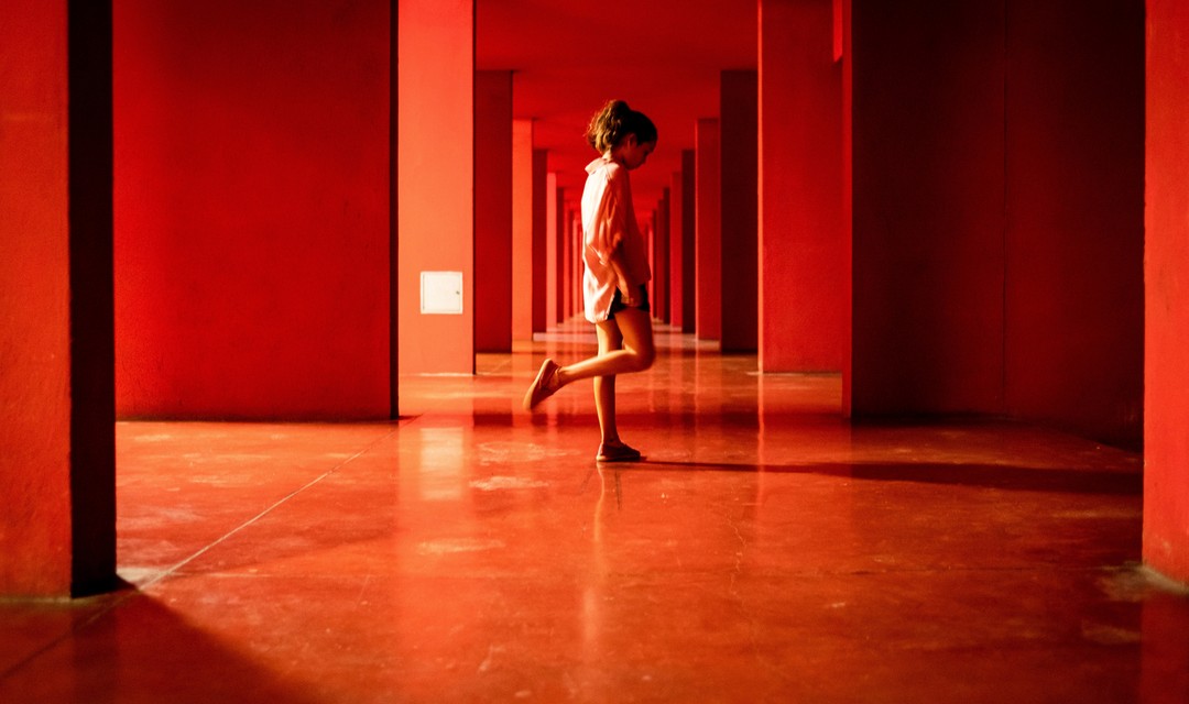 Maira Pia Pepe als Nika läuft barfuss durch einen rot beleuchteten Raum