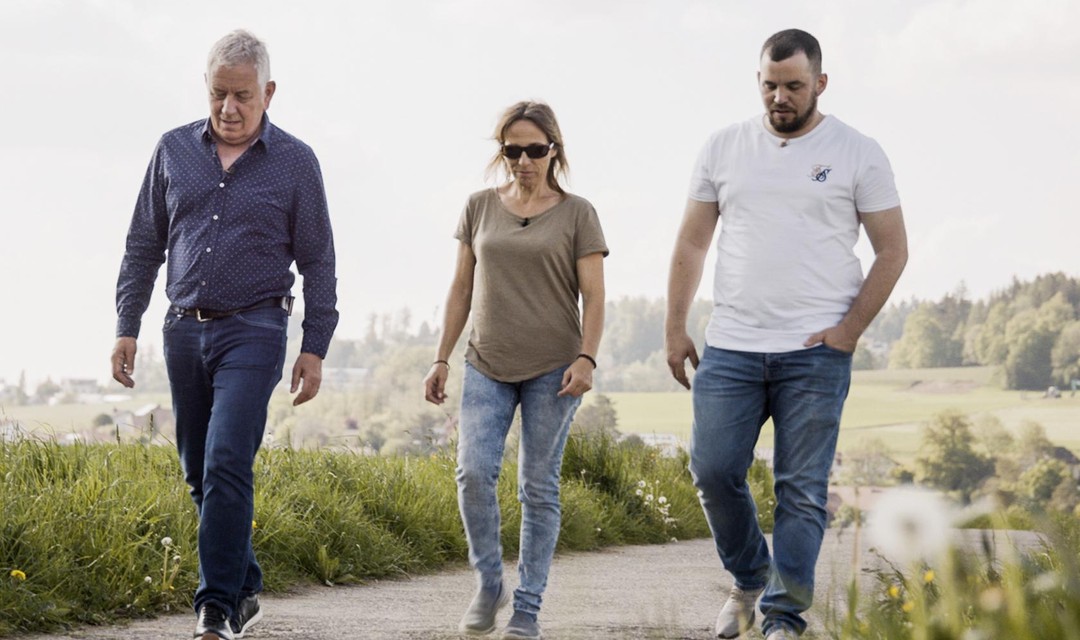 Röbi Koller läuft mit zwei Protagonist:innen auf einer Strasse