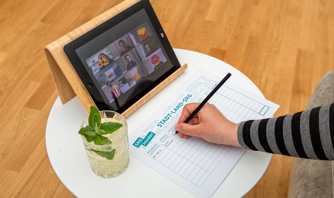 Jemand spielt im Wohnzimmer «Stadt, Land, SRG» und ist währenddem in einer Videokonferenz