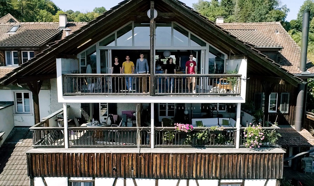 Ansicht Frontseite Haus. Auf dem oberen Balkon stehen die 5 Protagonistinnen und Protagonisten