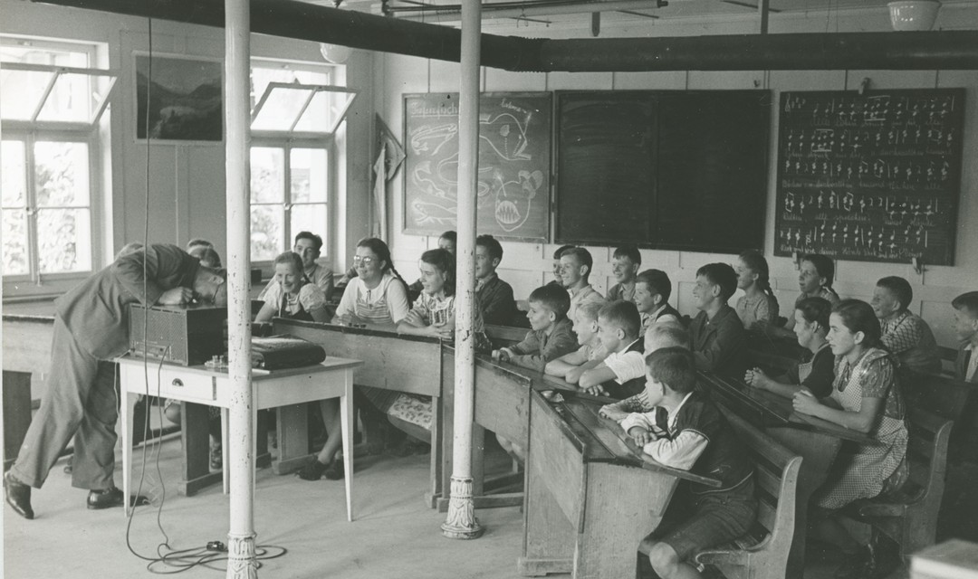 Ein altes Bild, indem ein Leher vor einer Klasse steht.