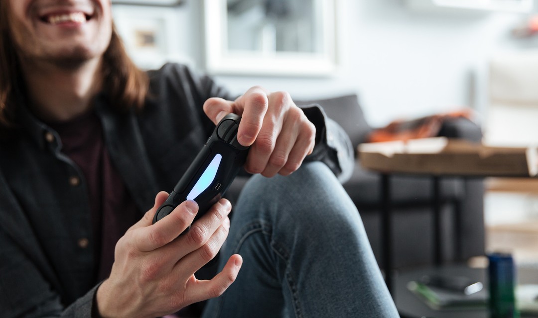 Ein Mann sitzt vor dem Sofa am Boden und spielt ein Game