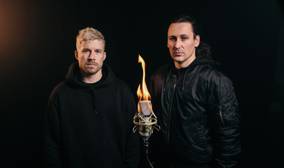 Die beiden Gastgeber Pablo Vögtli und Mauro Wolf stehen vor einem brennenden Mikrofon