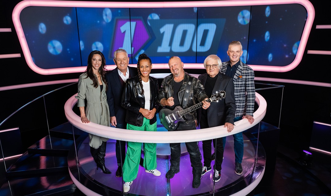 Foto: Kiki Maeder, Röbi Koller, Moderatorin Angélique Beldner, Gölä, Gilbert Gress und Rainer Maria Salzgeber stehen zusammen auf dem 1 gegen 100 Podium.