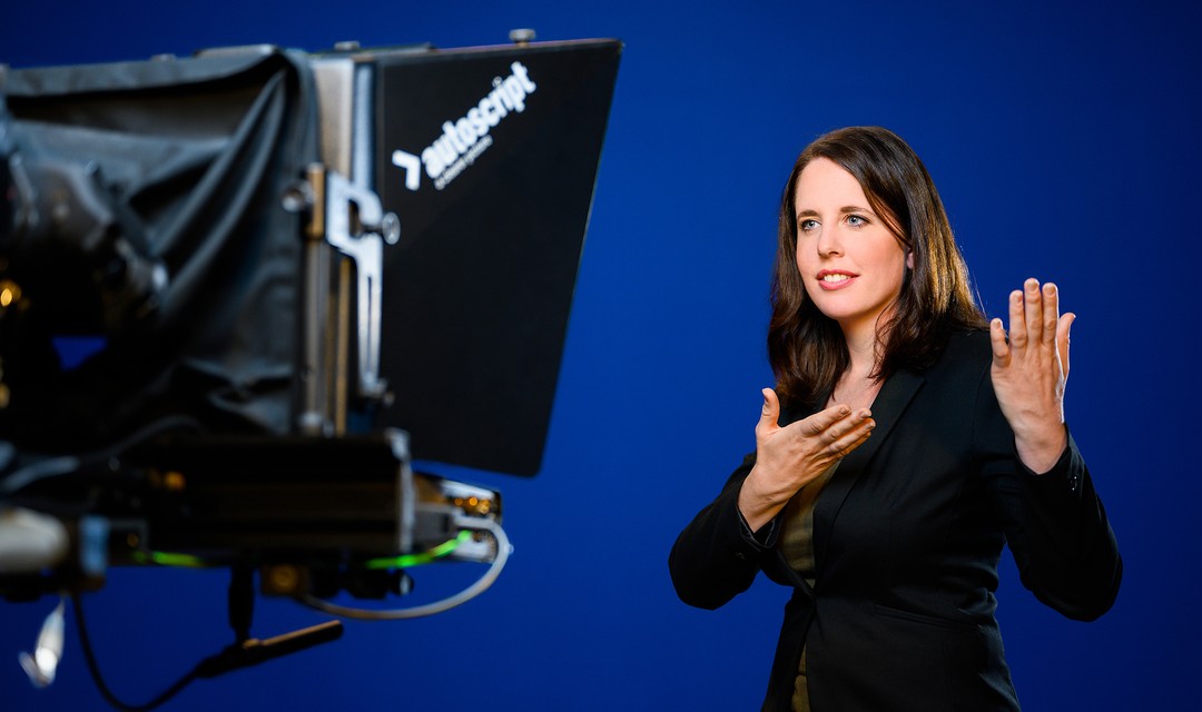 Eine Frau übersetzt vor einer Kamera in Gebärdensprache