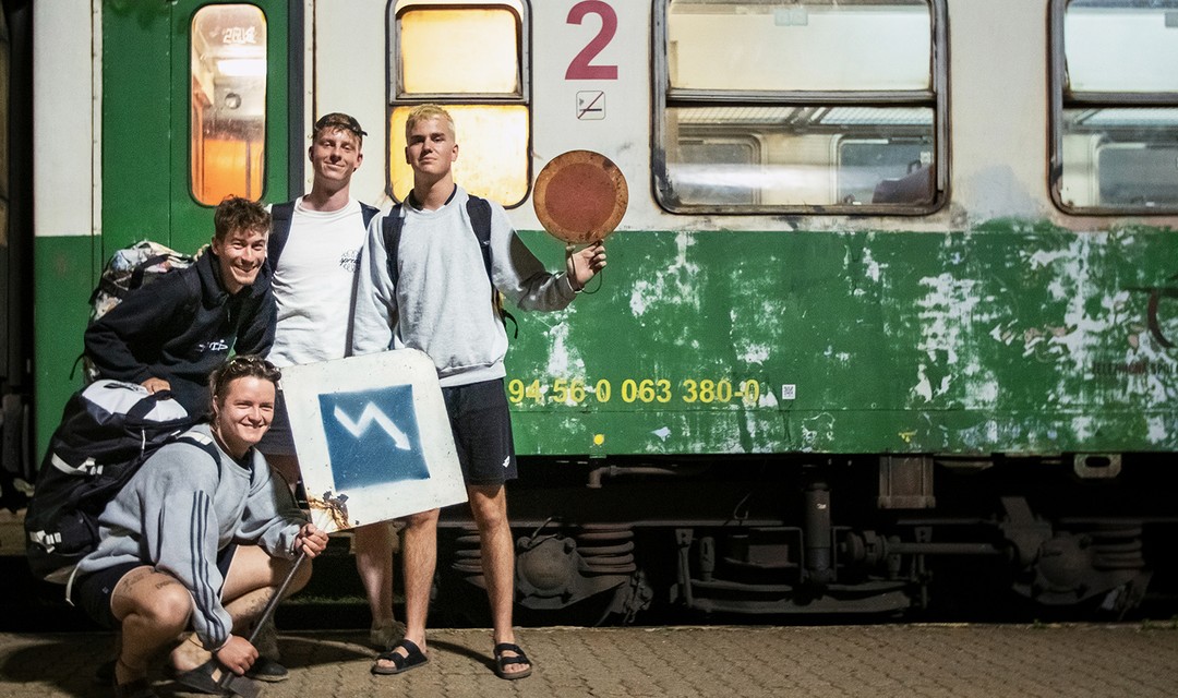 Vier Jungs posieren mit ihren Rucksäcken vor einem grünen Zug im Osten der Slovakei.