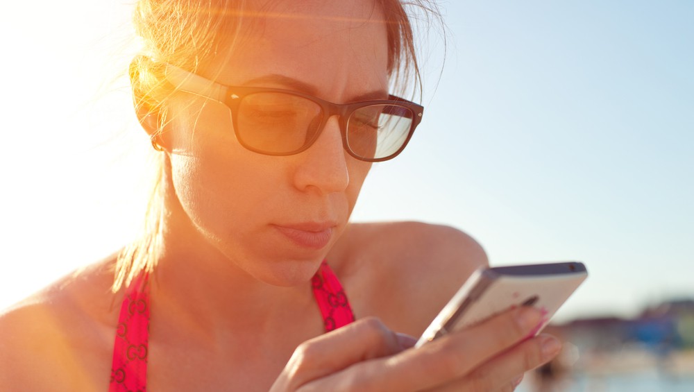 Frau mit Sonnenbrille schaut auf Handy