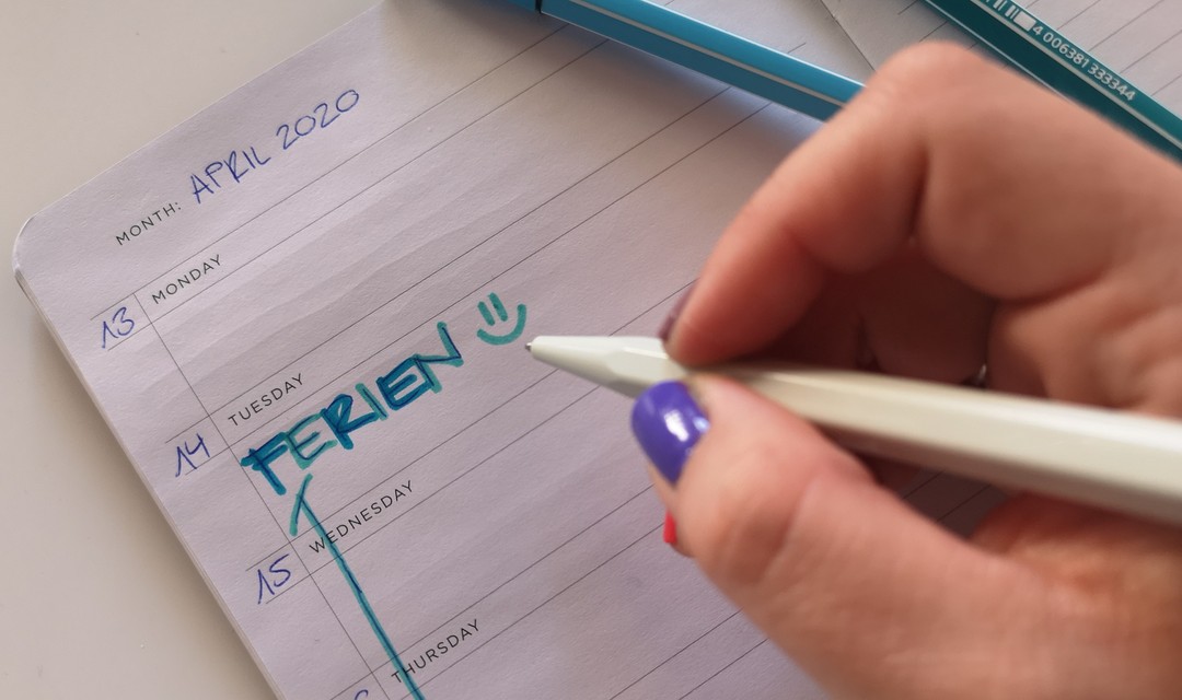 Eine Hand schreibt «Ferien» in die Agenda