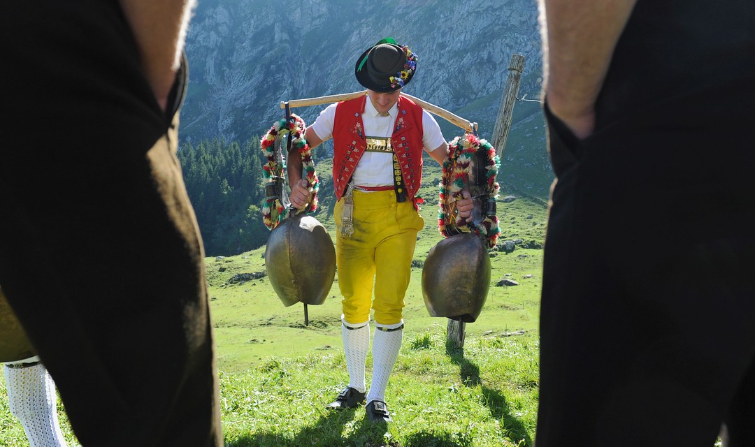 Foto eines Mannes in Tracht, der zwei Kuhglocken trägt