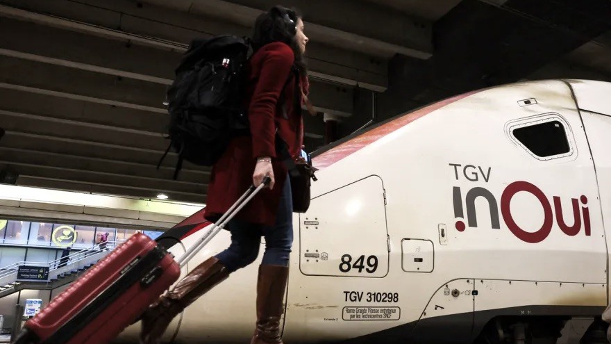 Frau läuft mit Rollkoffer vor einem TGV auf dem Bahnsteig