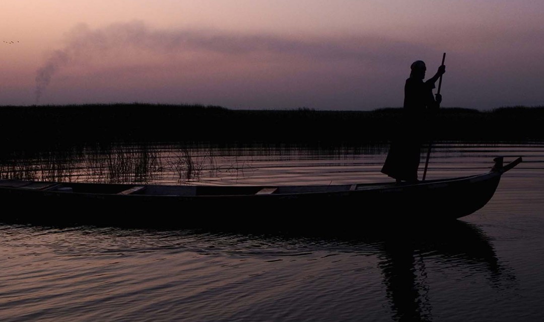 Foto: Ein Fährmann steht in der Dämmerung auf einem Boot auf einem Fluss.