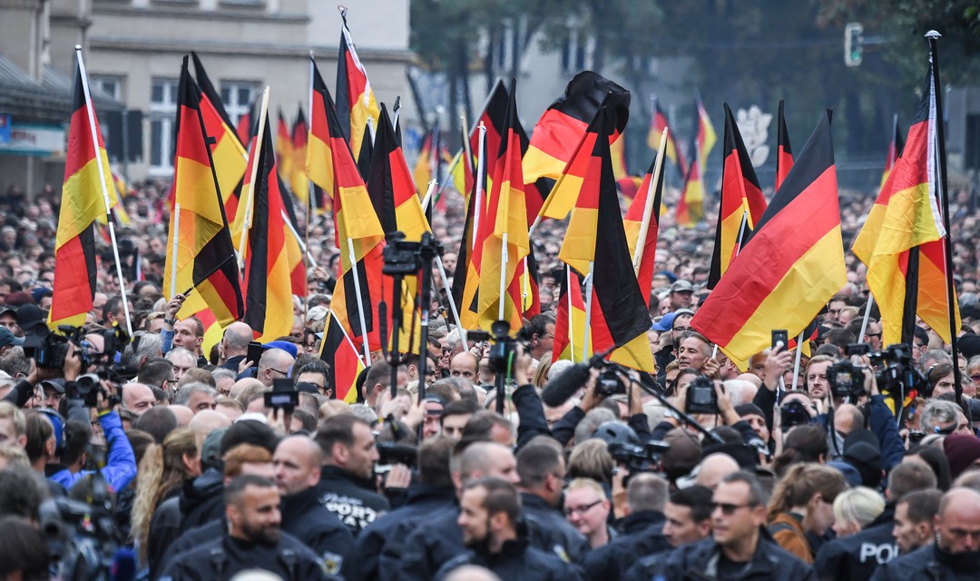 Draussen demonstrierende Menschen, vorwiegend Männer. Aus der Menge ragen viele Deutschland-Flaggen.