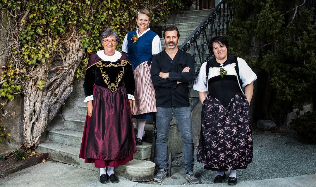 Vier Personen in Landtracht stehen vor einer Treppe und schauen in die Kamera.