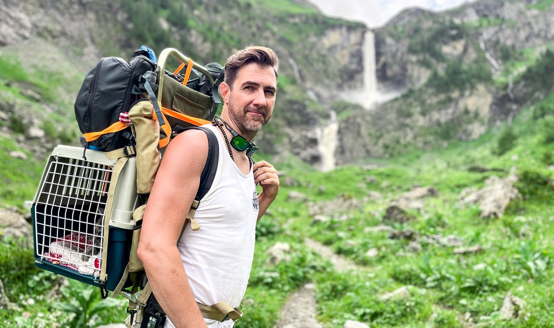 Foto Manu Burkart vor einem Wasserfall in den Bergen.