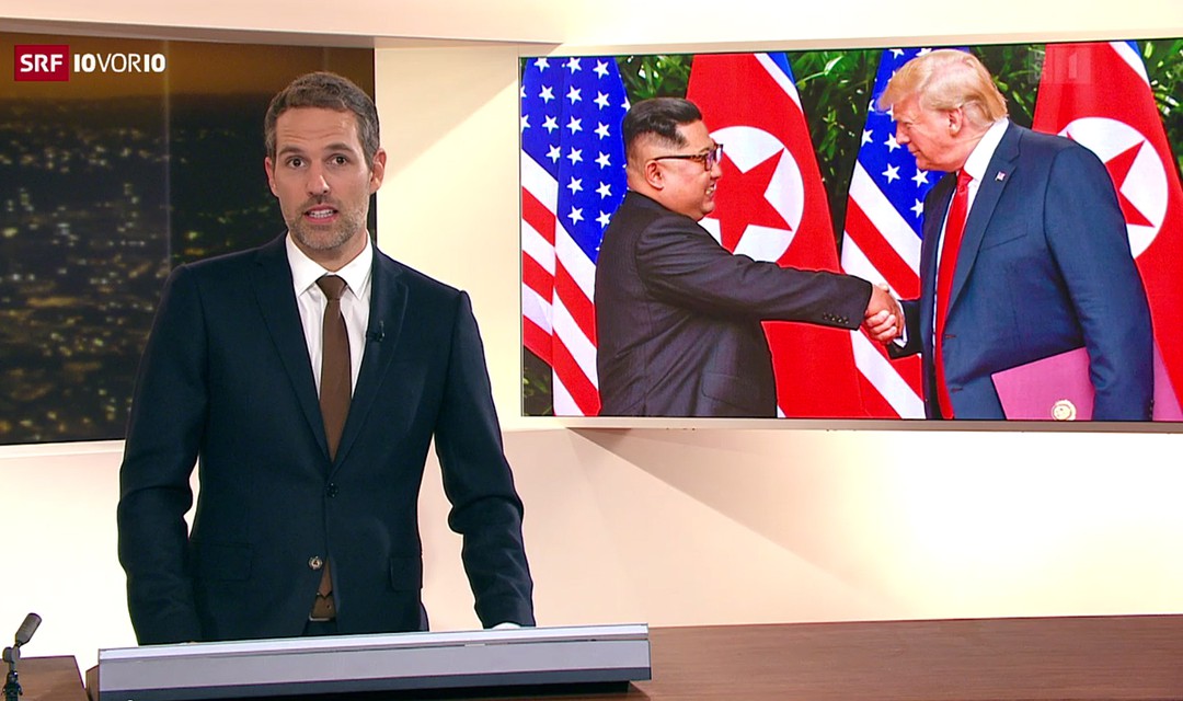 Moderator Arthur Honegger bei der Anmoderation, im Hintergrund Donald Trump und Kim Jong-un, die sich vor den beiden Landesflaggen die Hand schütteln