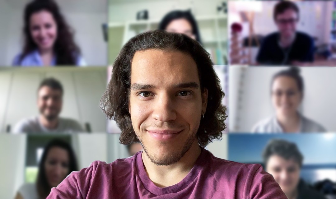 Jan schaut in die Kamera, im Hintergrund ist verschwommen ein Videocall.