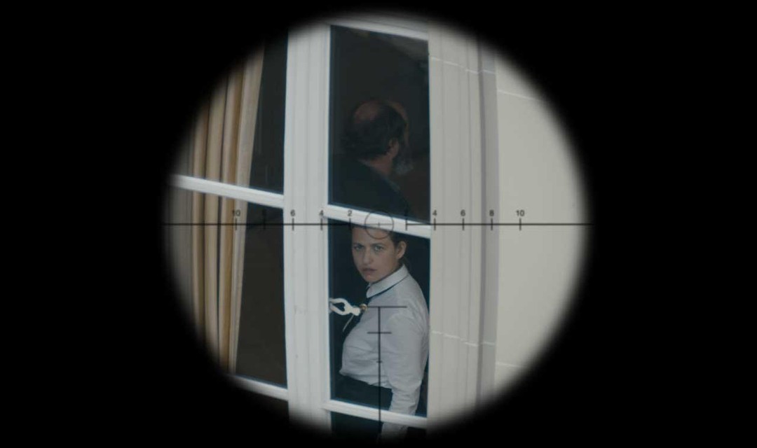 Durch den Sucher einer Waffe ist eine Frau zu sehen, die am Fenster steht