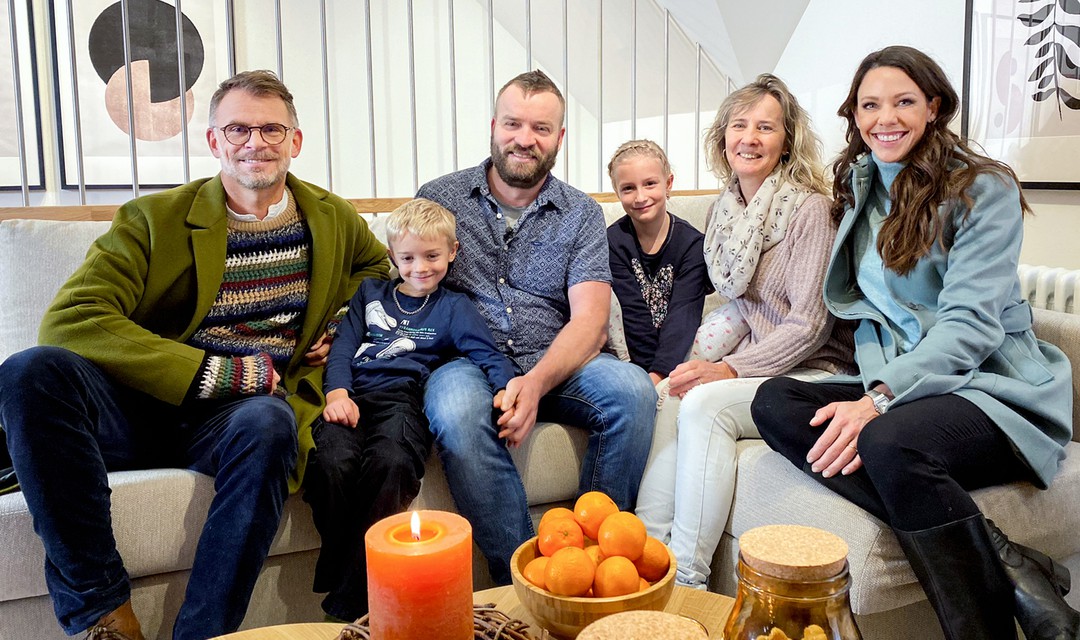 Andrin Schweizer und Kiki Maeder sitzen gemeinsam mit der Familie Hurni auf dem Sofa.