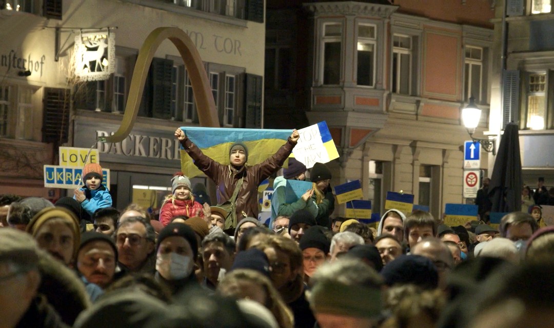 Bild einer Demonstration an der eine Ukraine- Flagge geschwenkt wird.