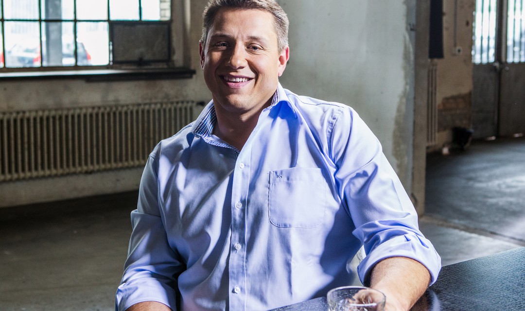 Jörg Abderhalden mit Glas in der Hand an Tisch sitzend