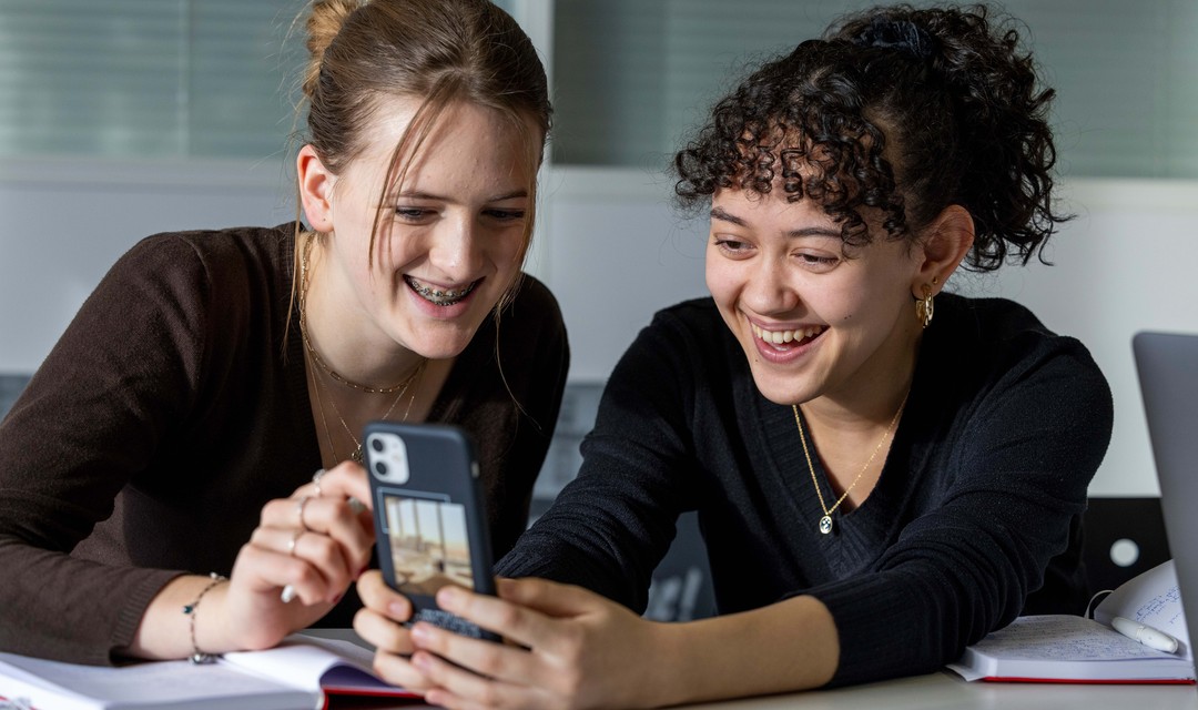 Foto von zwei Jugendlichen, die gemeinsam in ein Smartphone schauen.