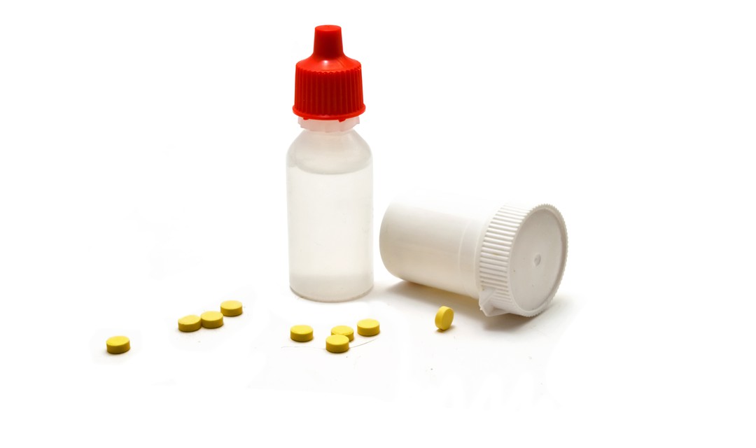 Becher mit gelben Pillen und Medikamentenglas mit Flüssigkeit