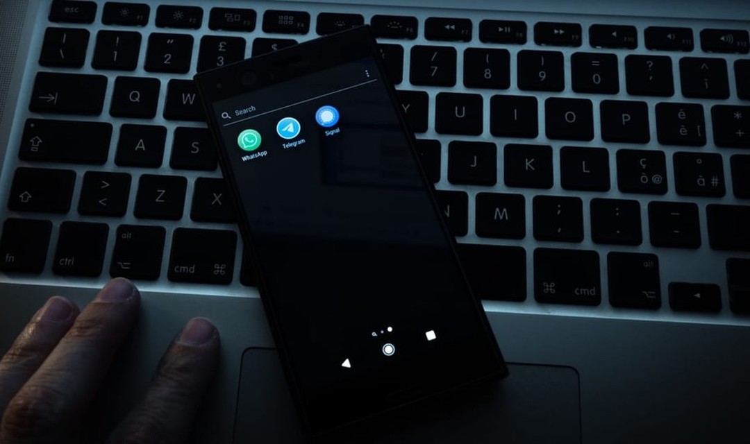 Ein Handy liegt auf einer Laptoptastatur, auf dem Apps von Messengerdiensten installiert sind