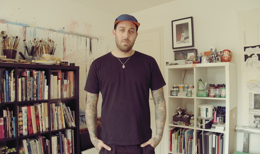 Tattookünstler Raphael blickt selbstbewusst in die Kamera. Er steht in seinem Tattoo-Studio.