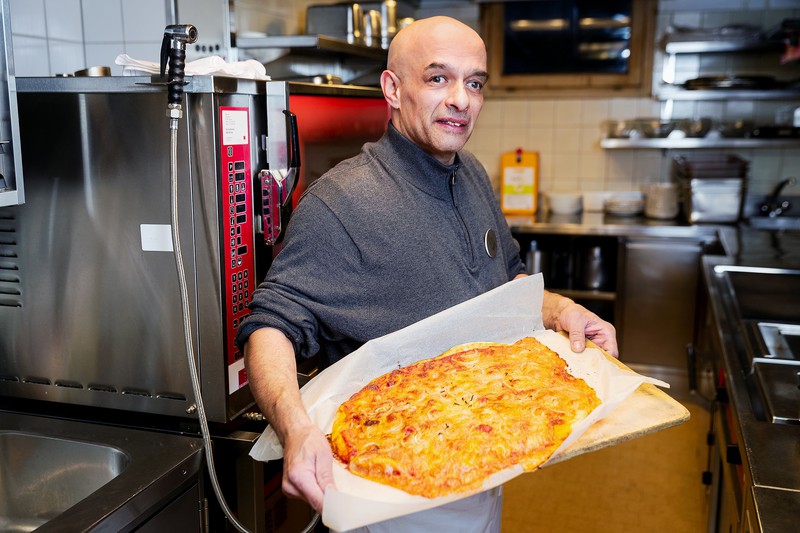 Ilker «Tony» Kivanc steht in der Hotelküche und präsentiert ein Blech mit einer frischen Pizza.