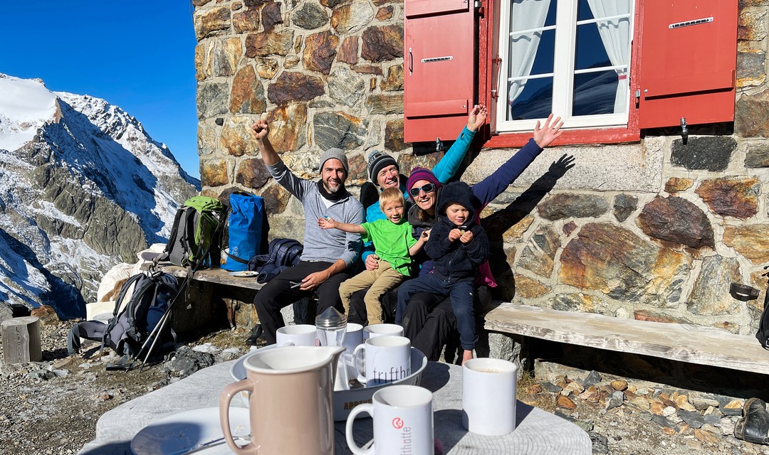 Manu Burkart sitzt mit der Hüttenwart-Familie vor der Trifthütte auf einer Bank.