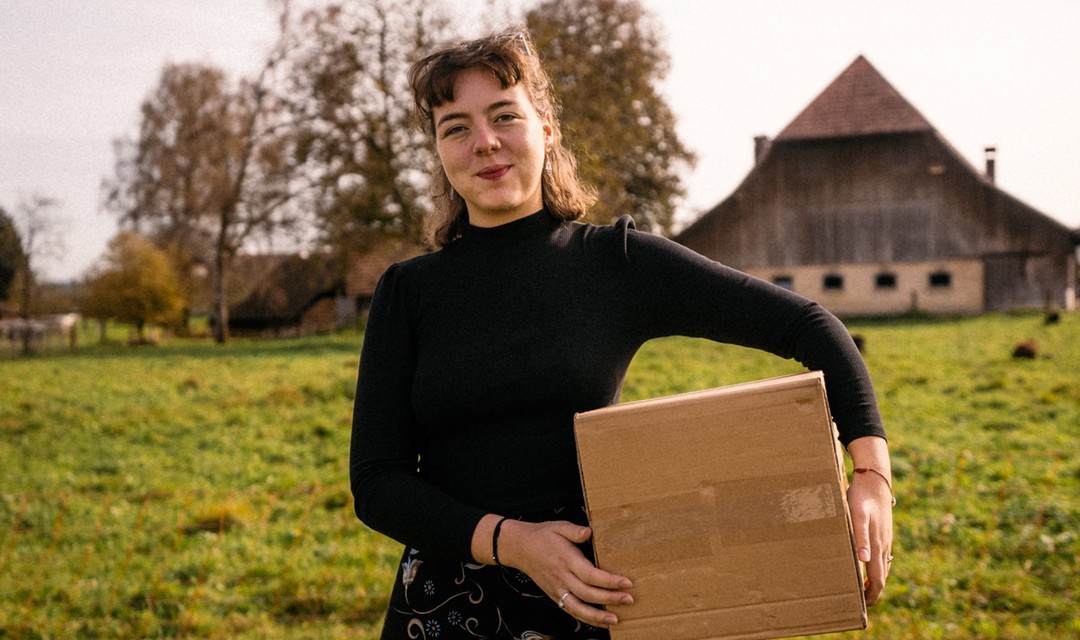 Eine Junge Frau hält einen Karton unter dem Arm und zieht von Zuhause aus.