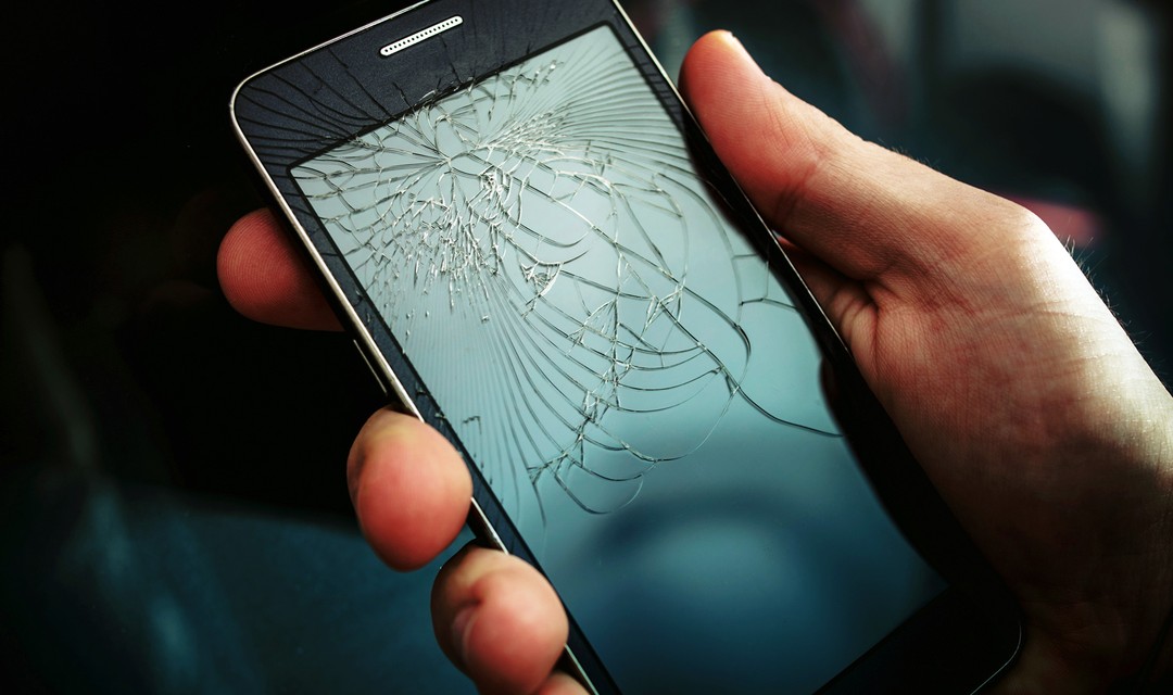 Jemand hält ein Smartphone mit einem zerbrochenen Bildschirm in der Hand