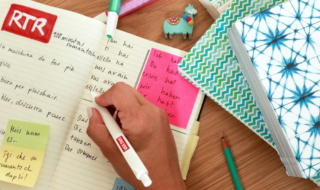 Auf einem kleinen Tisch ist ein Lernheft mit mehreren rätoromanischen Begriffen zu sehen.