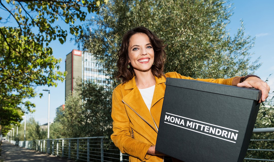 Mona Vetsch stehr vor dem SRF Gebäude in Leutschenbach und hält eine Überraschungsbox in der Hand