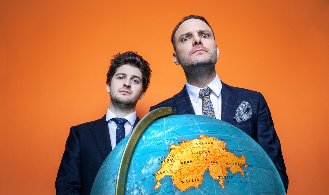 Dominic Deville und Patrick Karpiczenko stehen hinter einer Weltkugel