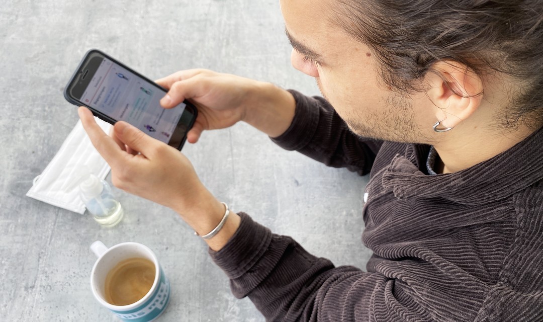 Overshoulder Blick: Jan sitzt auf der Terrasse und navigiert durch die SwissCovid-App.