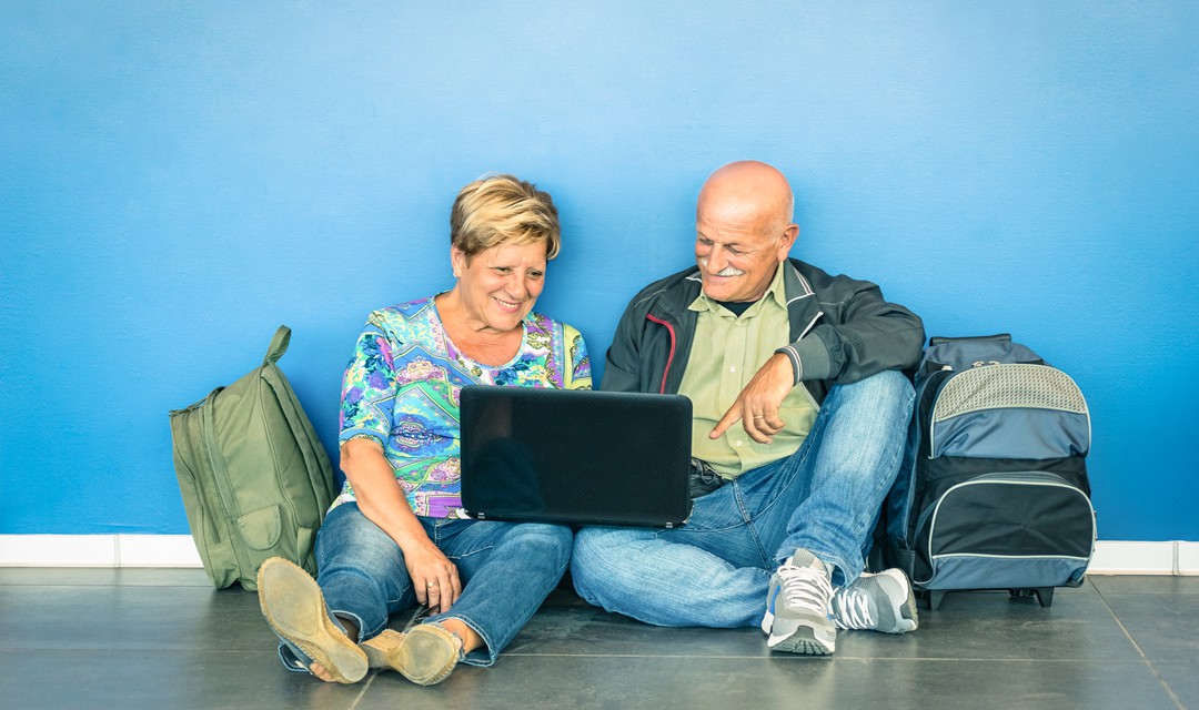 Zwei Senioren sitzen am Boden und schauen in einen Laptop.