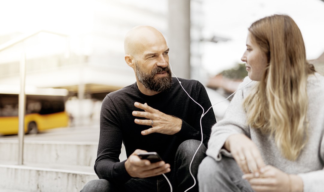 Ein Mann und eine Frau hören zusammen auf der Treppe mit Kopfhörern etwas auf dem Handy