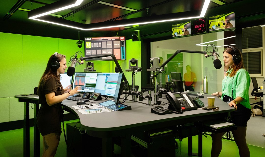 Moderatorin Mira Weingart und Produzentin Stephanie Brändle stehen im neuen Studio von SRF Virus vor dem Mikrofon