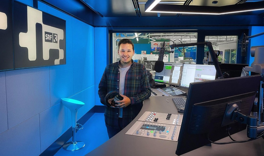 Joel Grolimund steht im SRF 3 Radiostudio mit Kopfhörern in der Hand