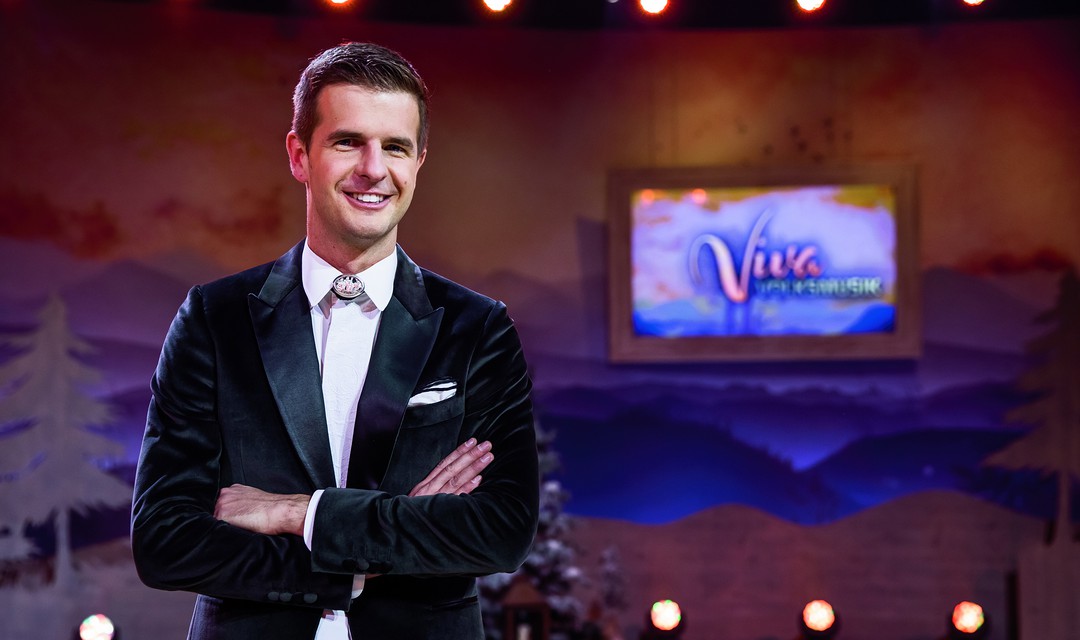 Nicolas Senn, Moderator von Viva Volksmusik, lächelt mit verschränkten Armen in die Kamera.