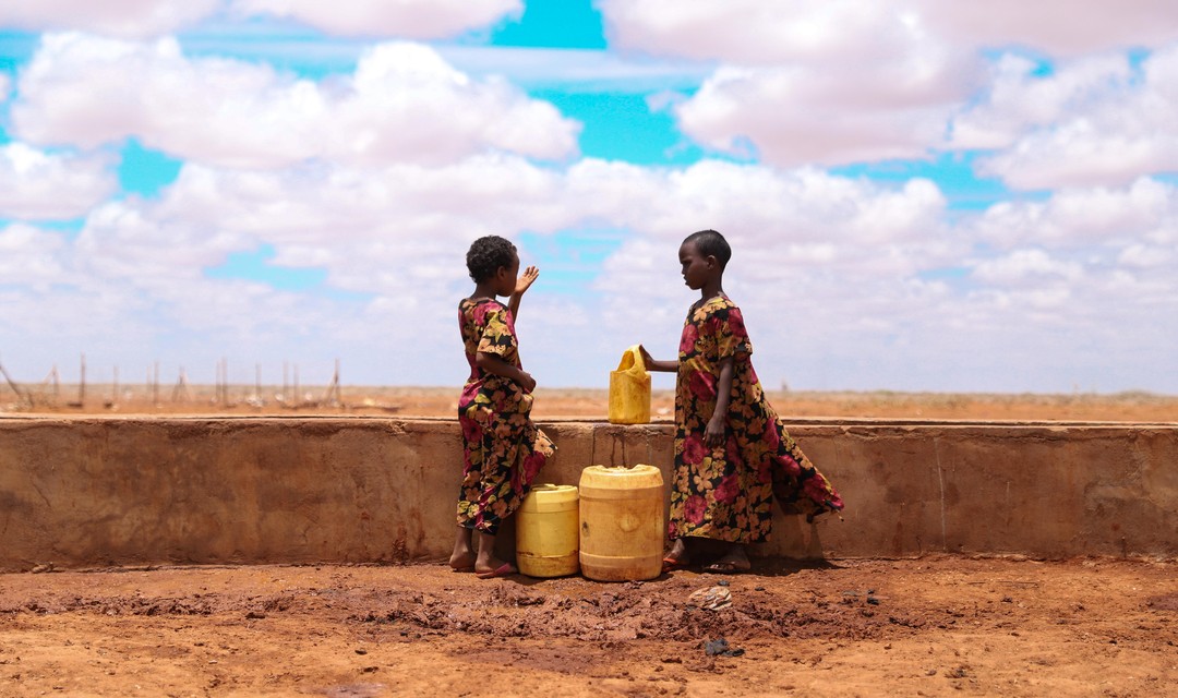 Zwei Kinder an einer Wasserstelle in Kenia, rundherum ist eine karge Wüstenlandschaft.