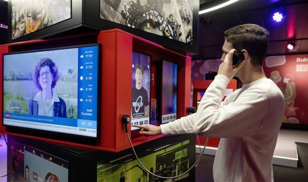 Bild einer Person die vor einem Bildschirm steht und ein Telefonhörer in der Hand hat
