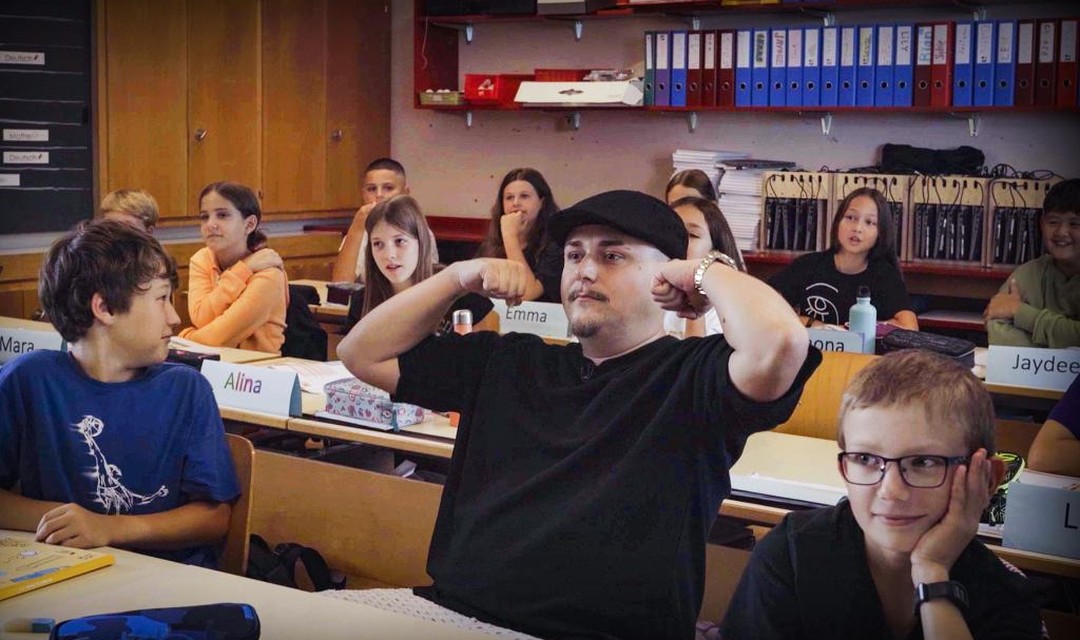 Rapper EAZ sitzt mitten im schulzimmer mit schulkindern