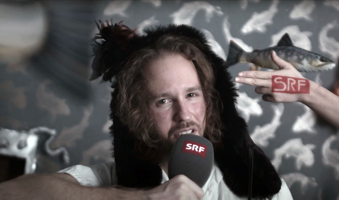 Host Jan Tukan mit dem SRF-Mikrofon vor einem Aquarium-Hintergrund