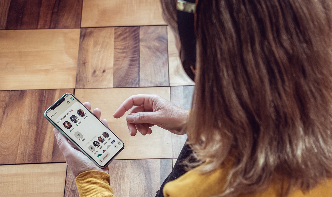 Eine Frau mit Kopfhörern auf schaut auf ihr Handy, geöffent ist die App Clubhouse.